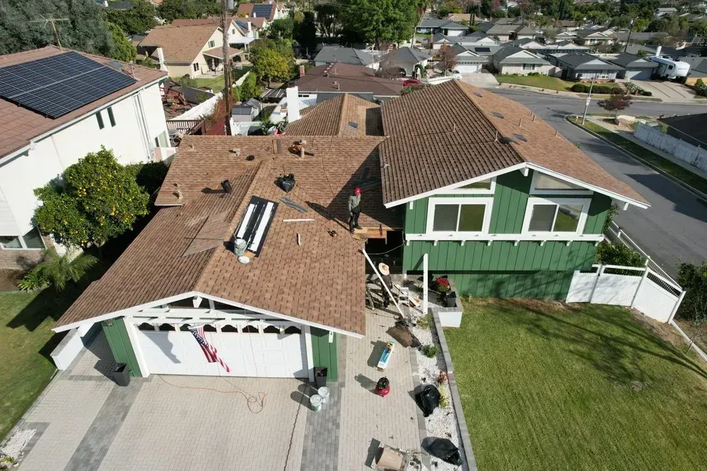 Aerial view of a residential house with a shingled roof under construction, featuring a worker on a ladder in the front.