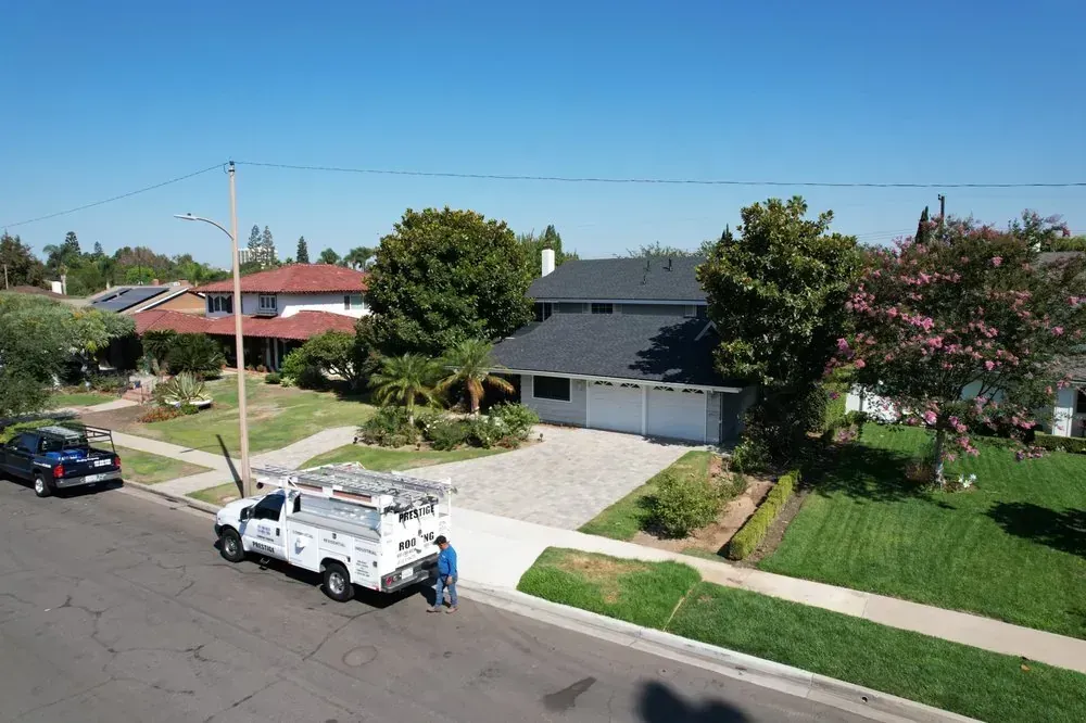 A utility truck parked on a suburban street in front of a house with a gray roof and a white garage.