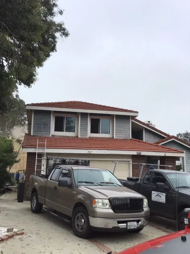 A two-story house with a terracotta tile roof and grey siding, featuring two parked pickup trucks in the driveway.