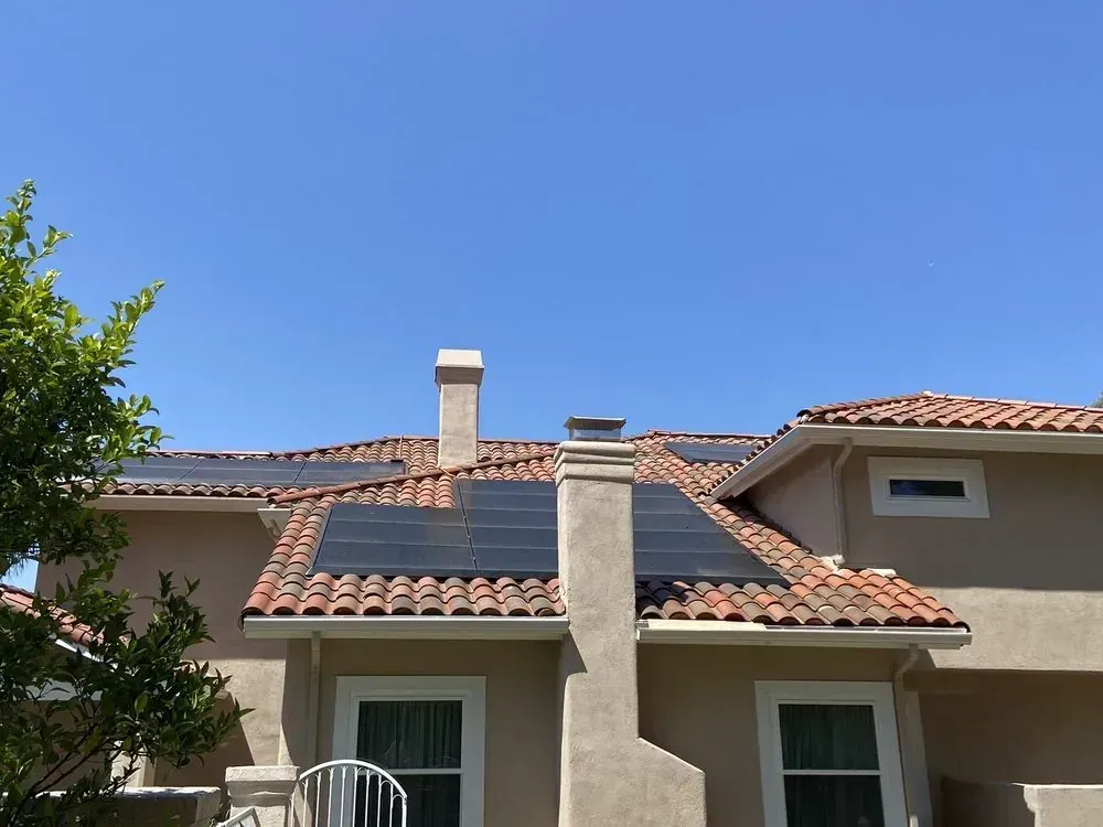 Solar panels installed on the roof of a house with terracotta tiles under a clear blue sky.