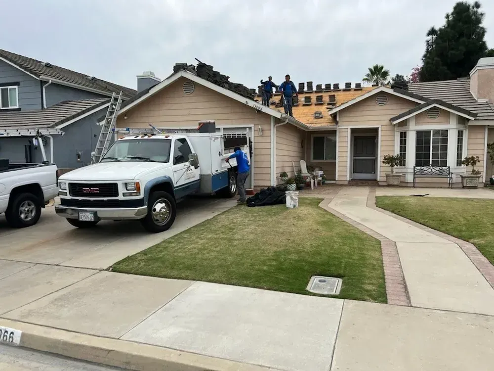 Contractors working on the roof of a suburban home, with a utility truck parked in the driveway.