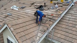 A worker wearing a blue shirt installs roofing tiles on a house roof.