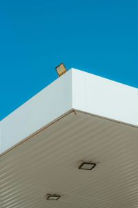 A white, overhanging canopy corner against a bright blue sky, with three rectangular light fixtures visible.