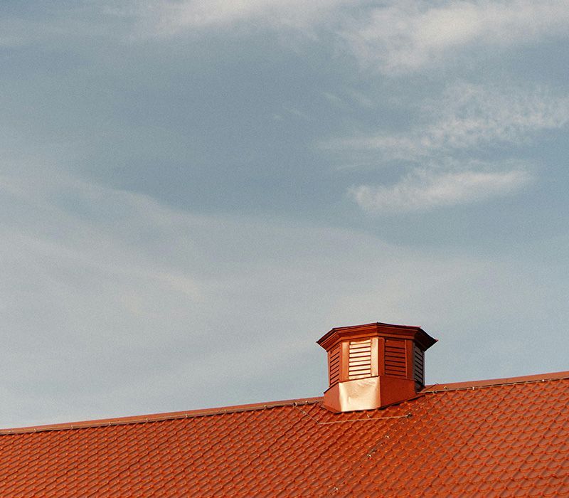 A red metal roof with a louvered cupola against a blue sky with wispy white clouds.