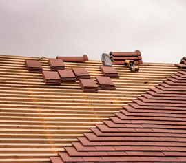 A roof undergoing renovation with rows of red clay tiles partially installed over wooden battens.