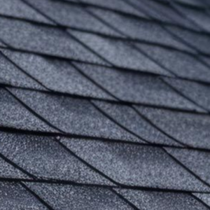 A close-up view of dark grey asphalt shingles on a residential roof, showing their overlapping, textured pattern.