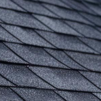 A close-up view of dark grey asphalt shingles on a residential roof, showing their overlapping, textured pattern.