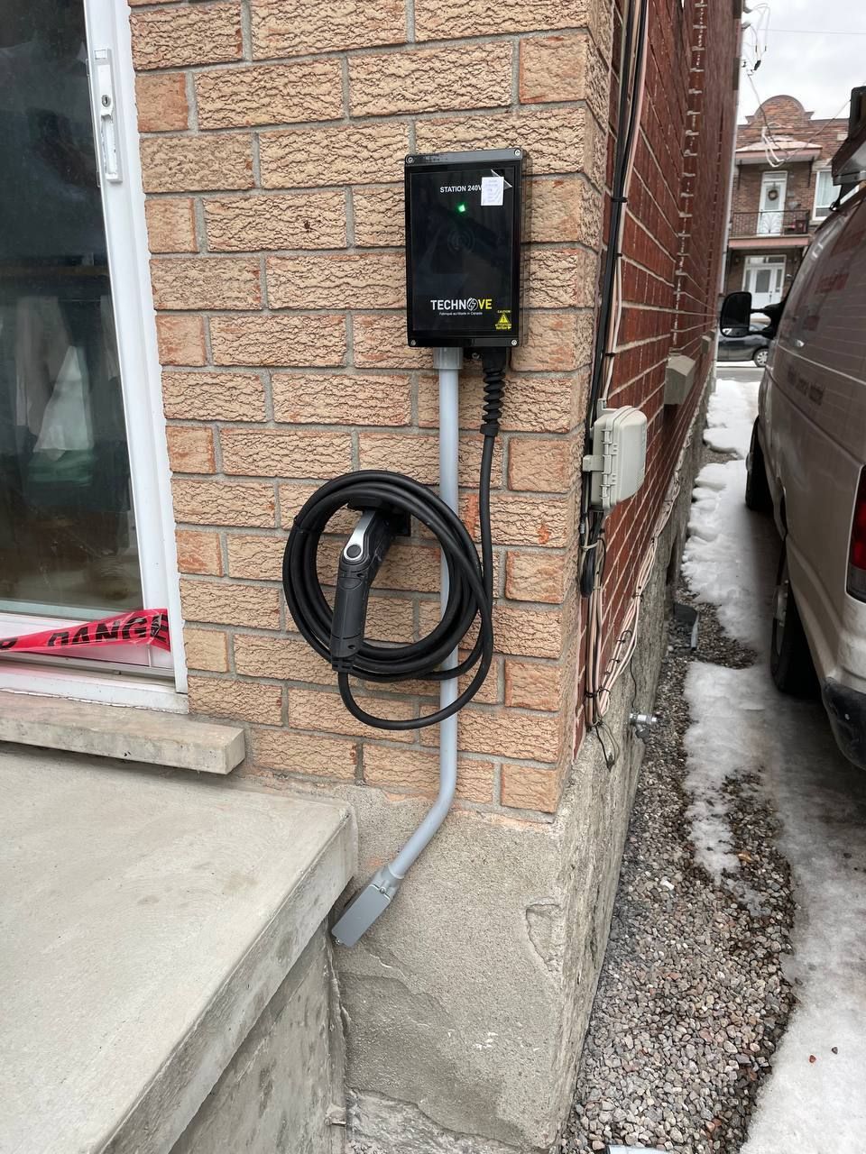 A car charger is attached to the side of a brick building.