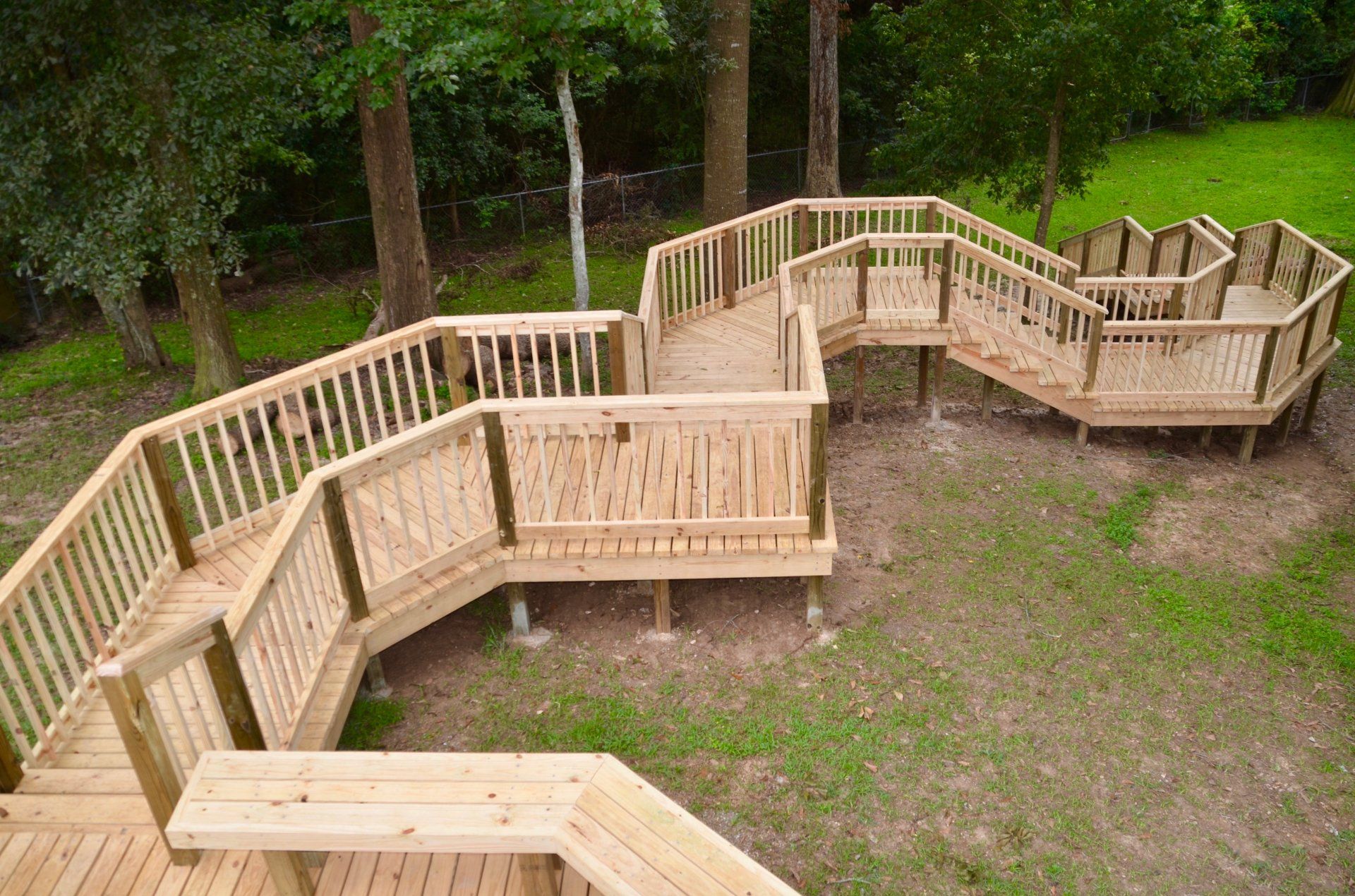 Wooden outdoor staircase winding down a grassy hillside, surrounded by trees.