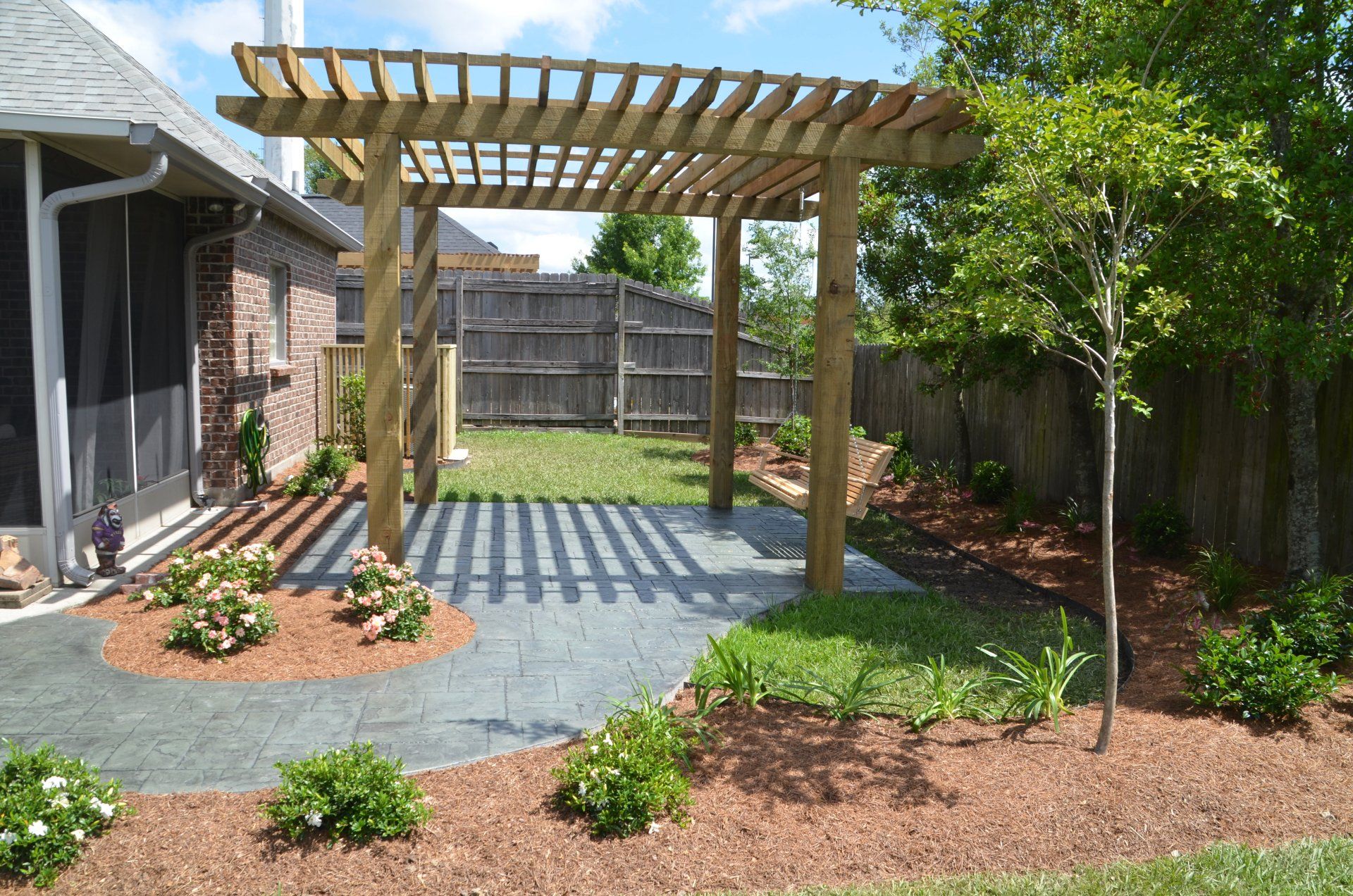 Wooden pergola over a patio in a backyard with landscaping.