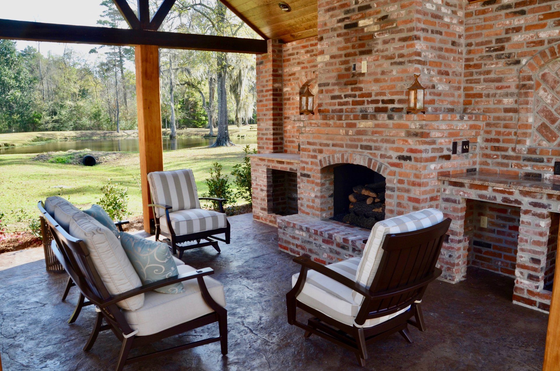Outdoor brick fireplace with seating area overlooking a green yard and trees.