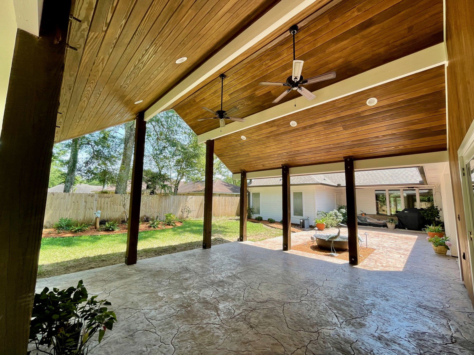 Covered patio with wood ceiling, ceiling fans, and stamped concrete floor overlooking a backyard.