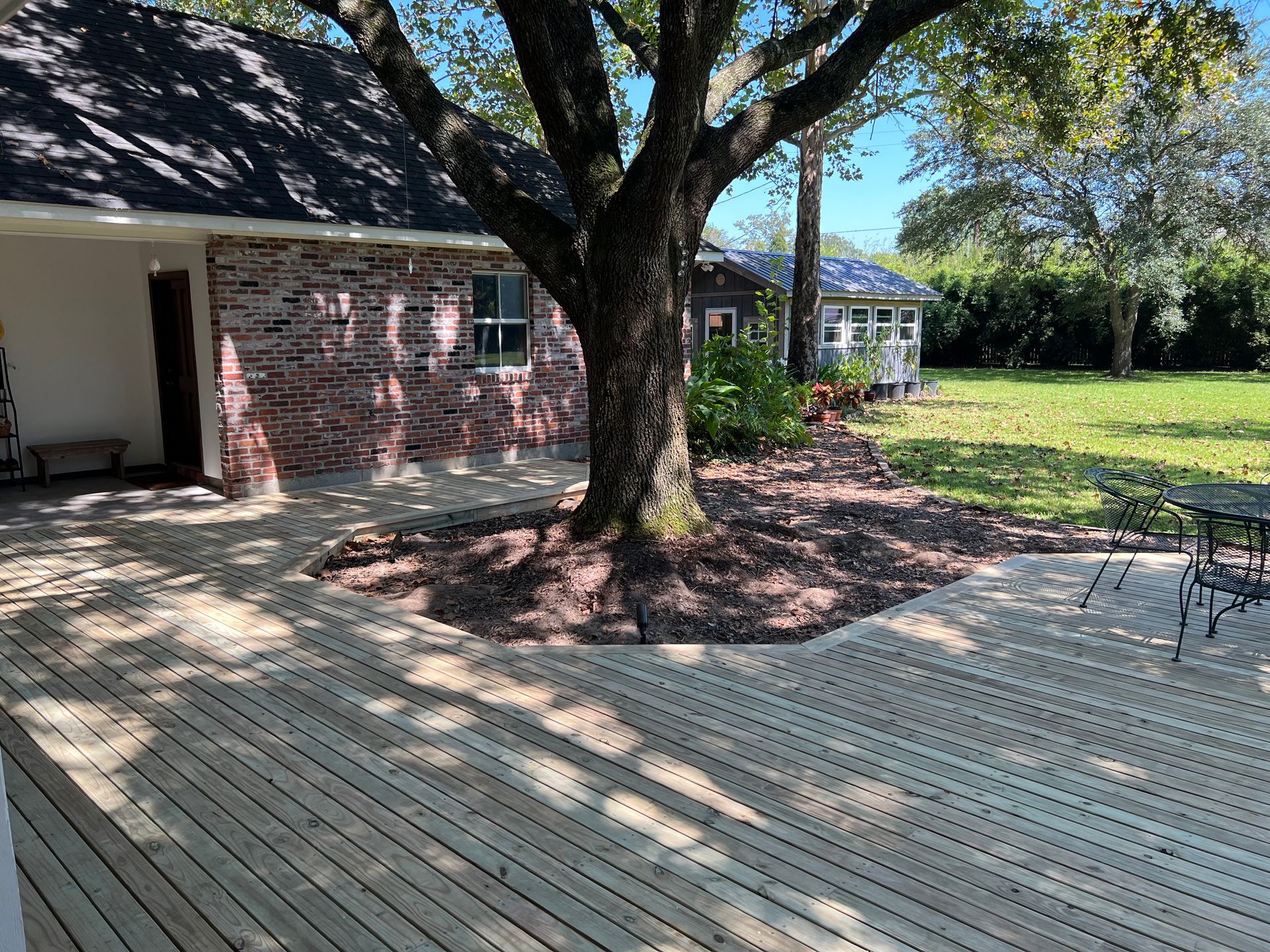Wooden deck with tree and brick house. Gazebo in background, grass and landscaping.