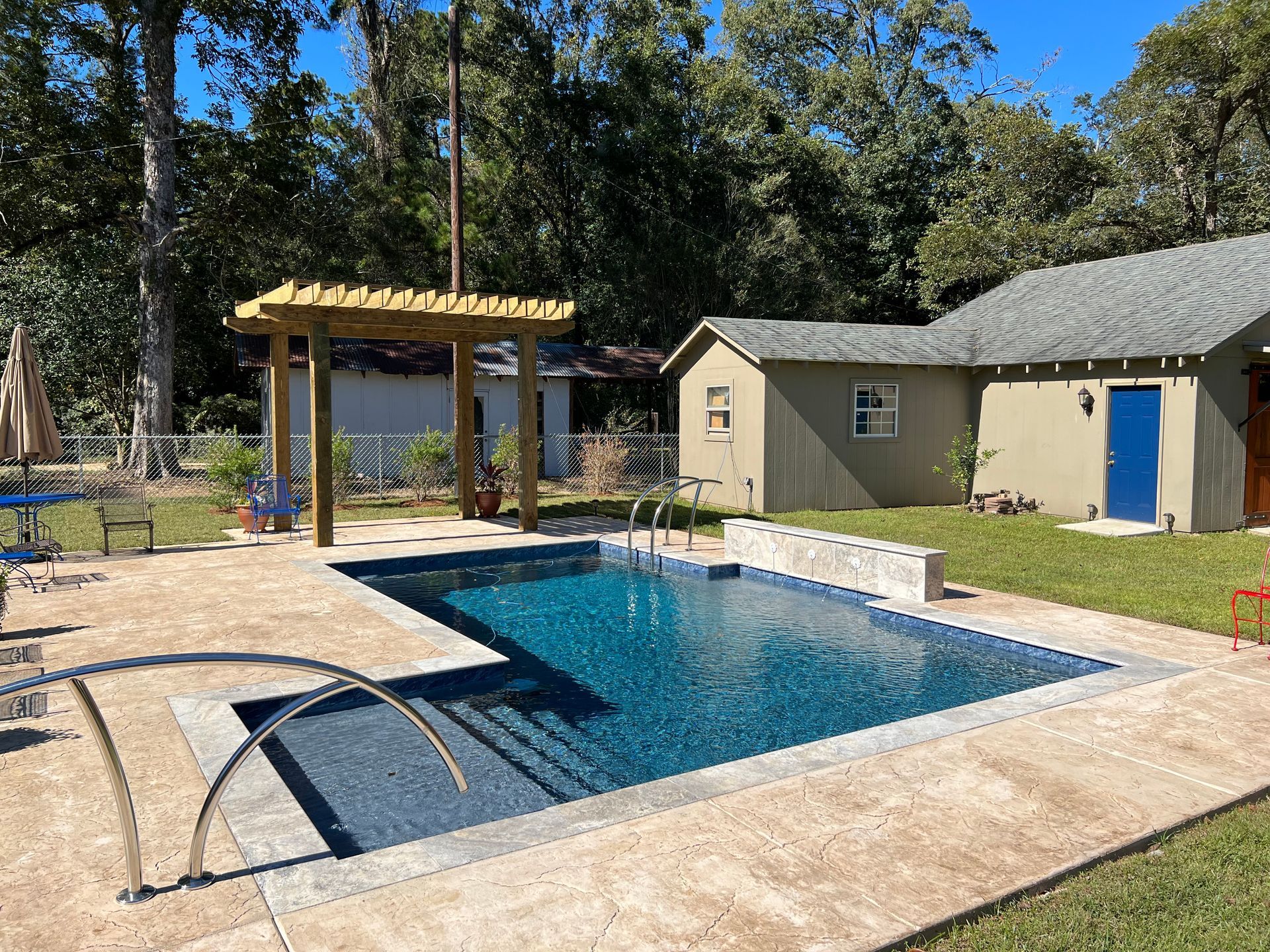 A backyard with a rectangular pool, pergola, and small structures on a sunny day.