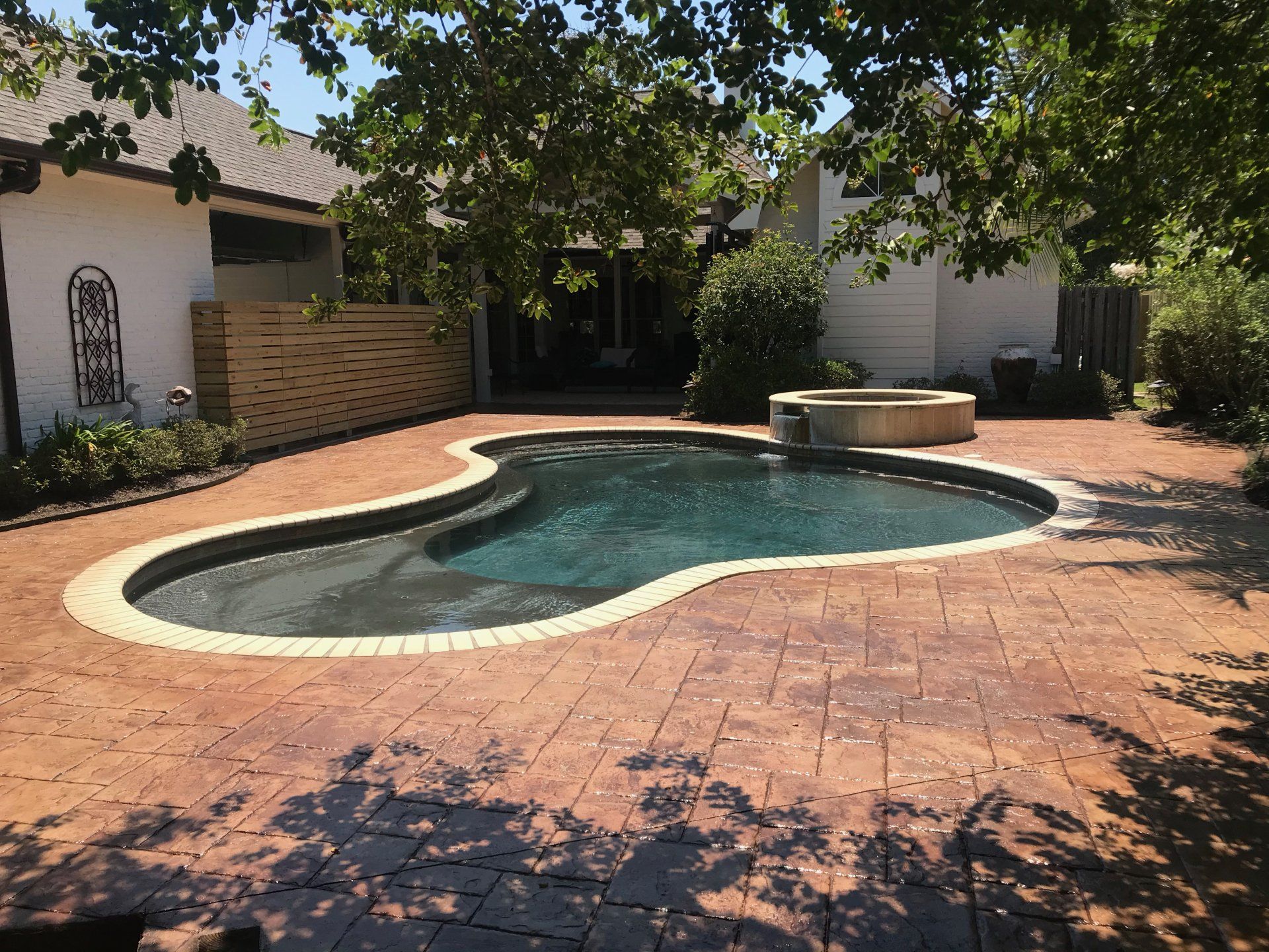 Backyard with a dark-blue, kidney-shaped pool, surrounded by red brick, trees, and a spa.