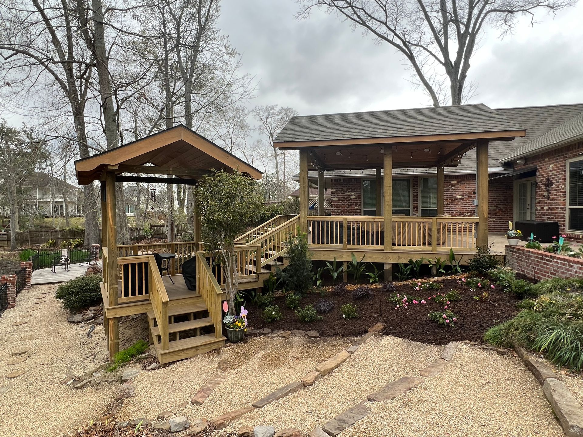 Wooden decks with roofs, steps, and railings, surrounded by landscaping, under an overcast sky.