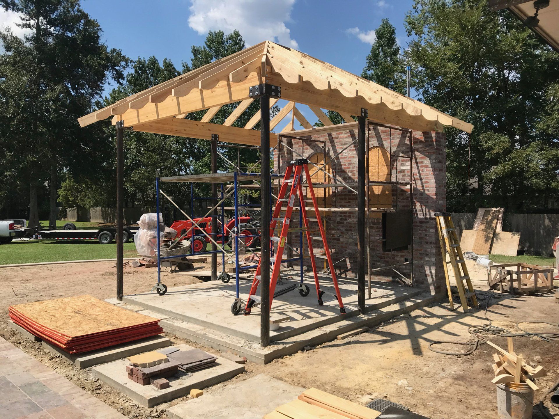 Construction of an outdoor brick structure with a wooden roof, scaffolding, and tools.