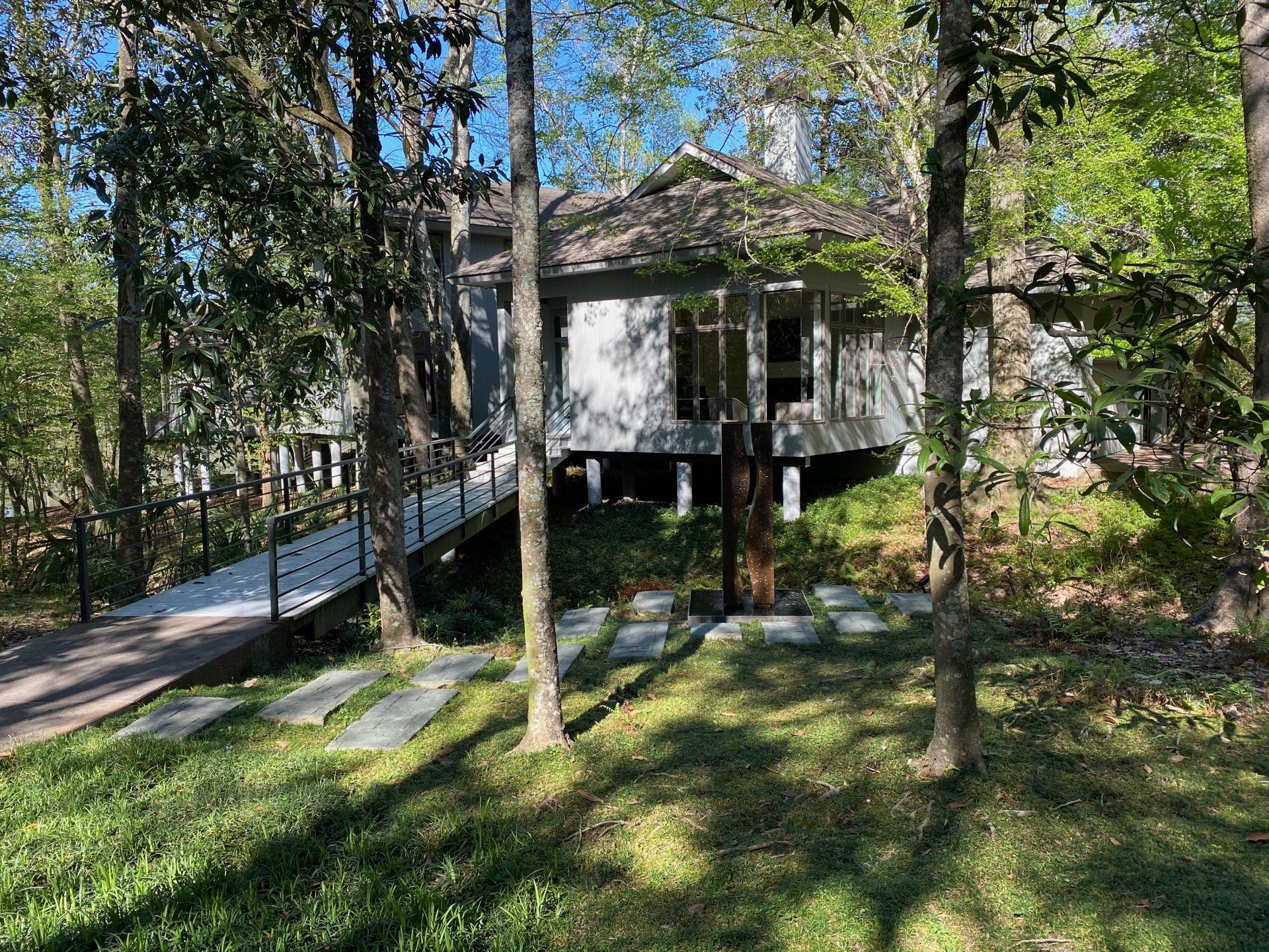 A white house on stilts in a forest, with a walkway leading to the entrance.