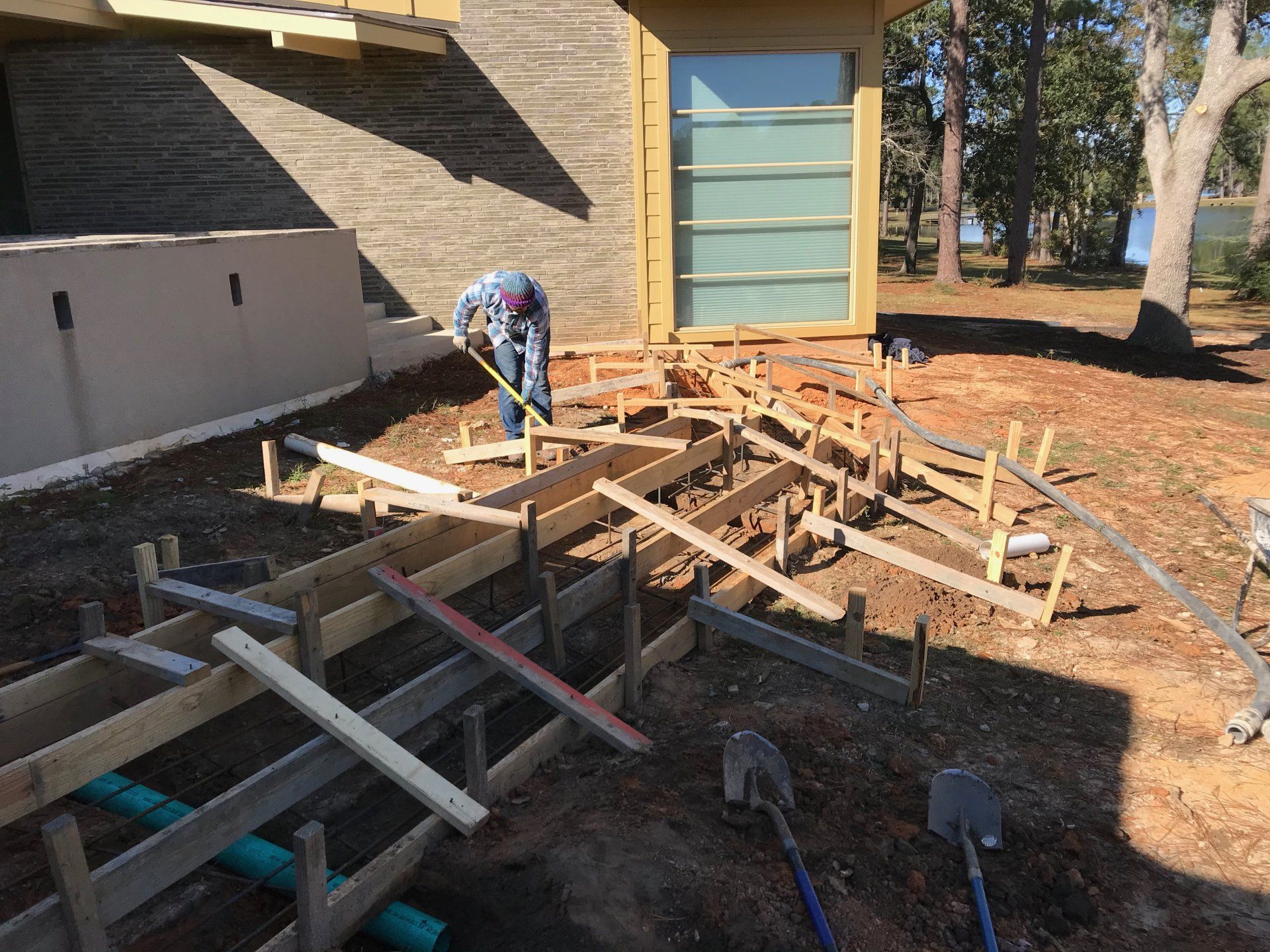 Construction worker measuring wooden forms for a concrete walkway outdoors.