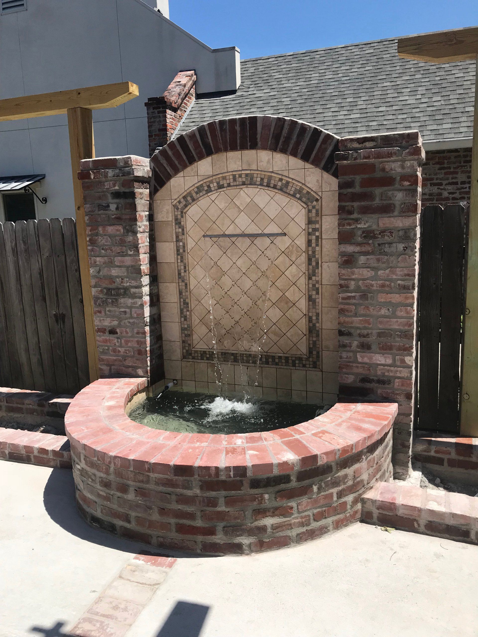 Brick water fountain with tiled backing, arch, and basin; wooden supports on either side.