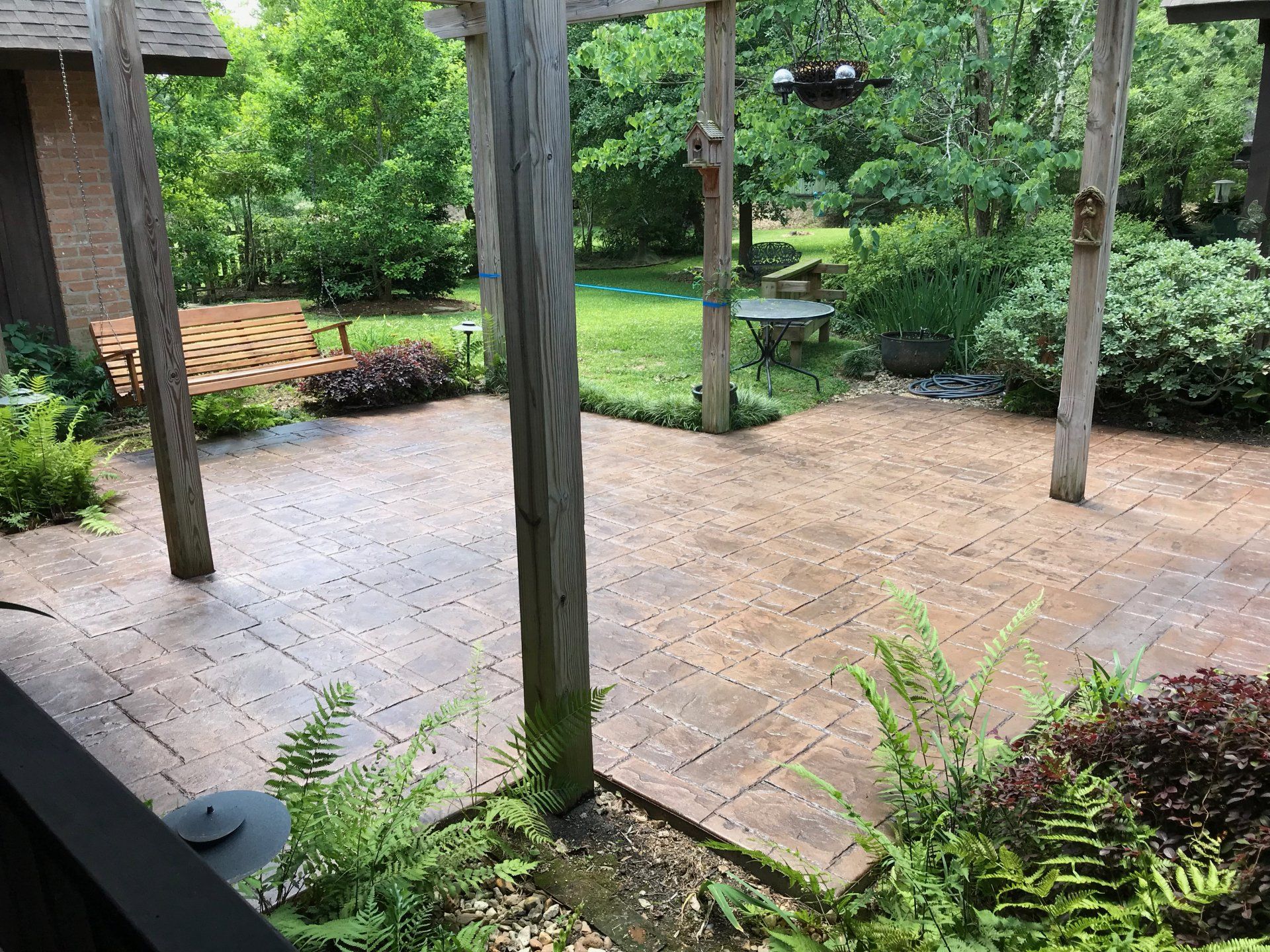 Patio with stamped concrete, surrounded by greenery and wooden posts, leading to a lawn.