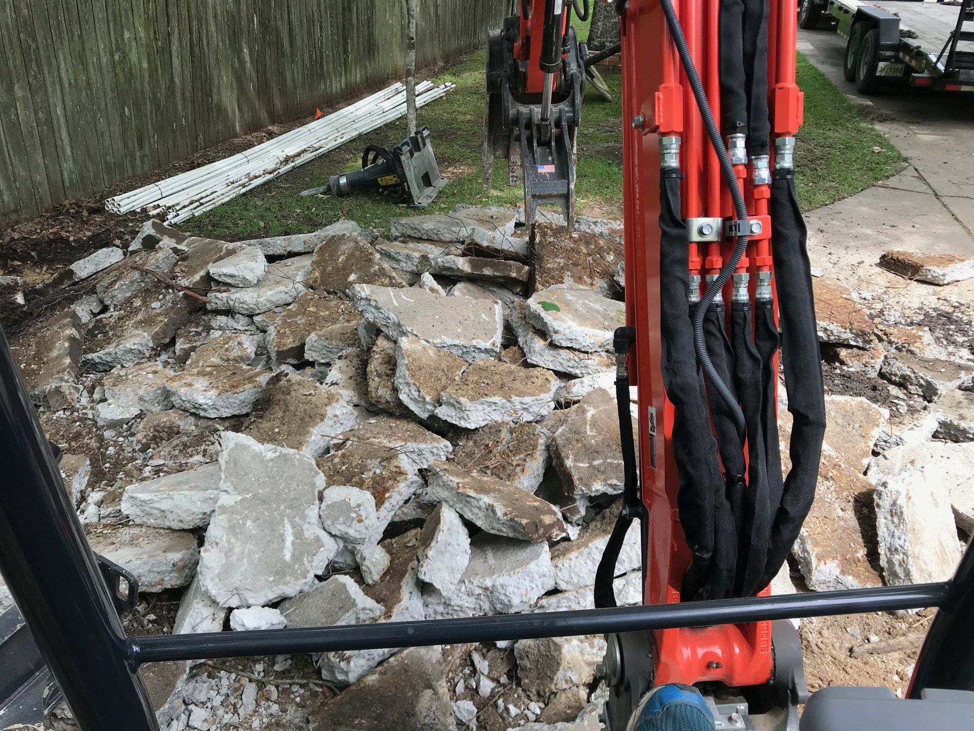 Excavator breaking concrete slabs in a yard. Red and black equipment.