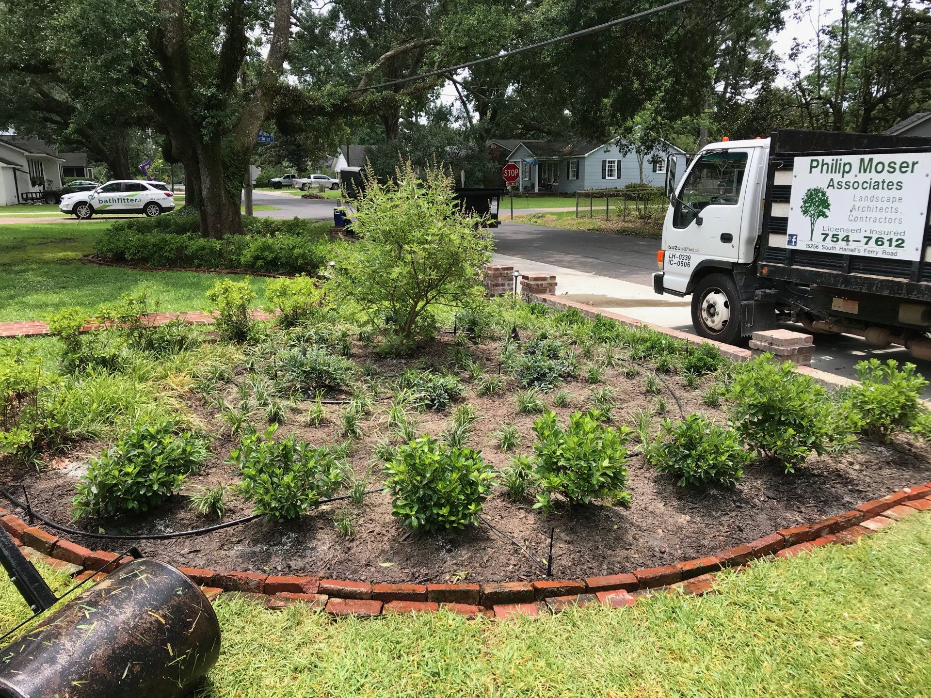 Landscaped garden bed with shrubs and a tree, edged with red bricks, next to a truck.