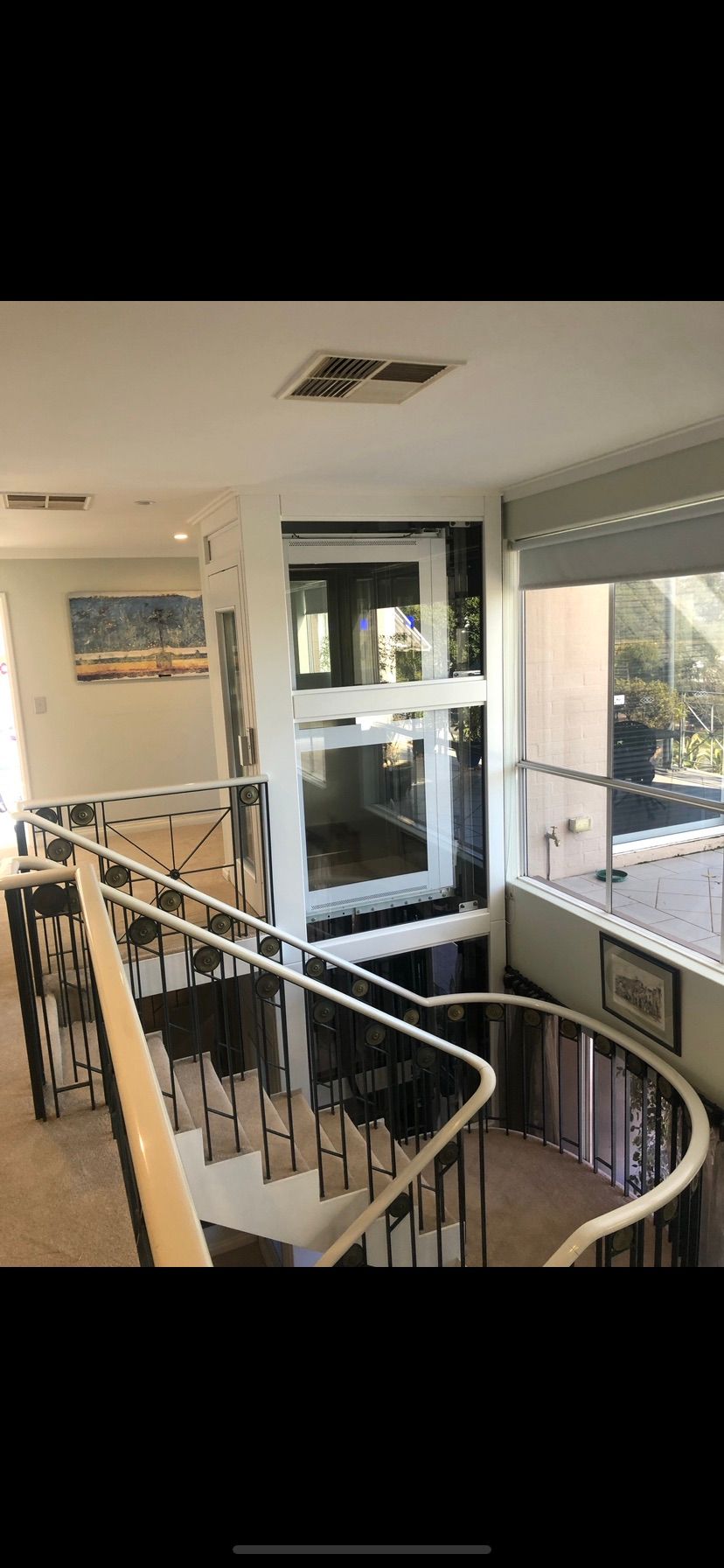 Interior view of a staircase and a glass elevator in a home. The staircase has a curved railing and black accents.