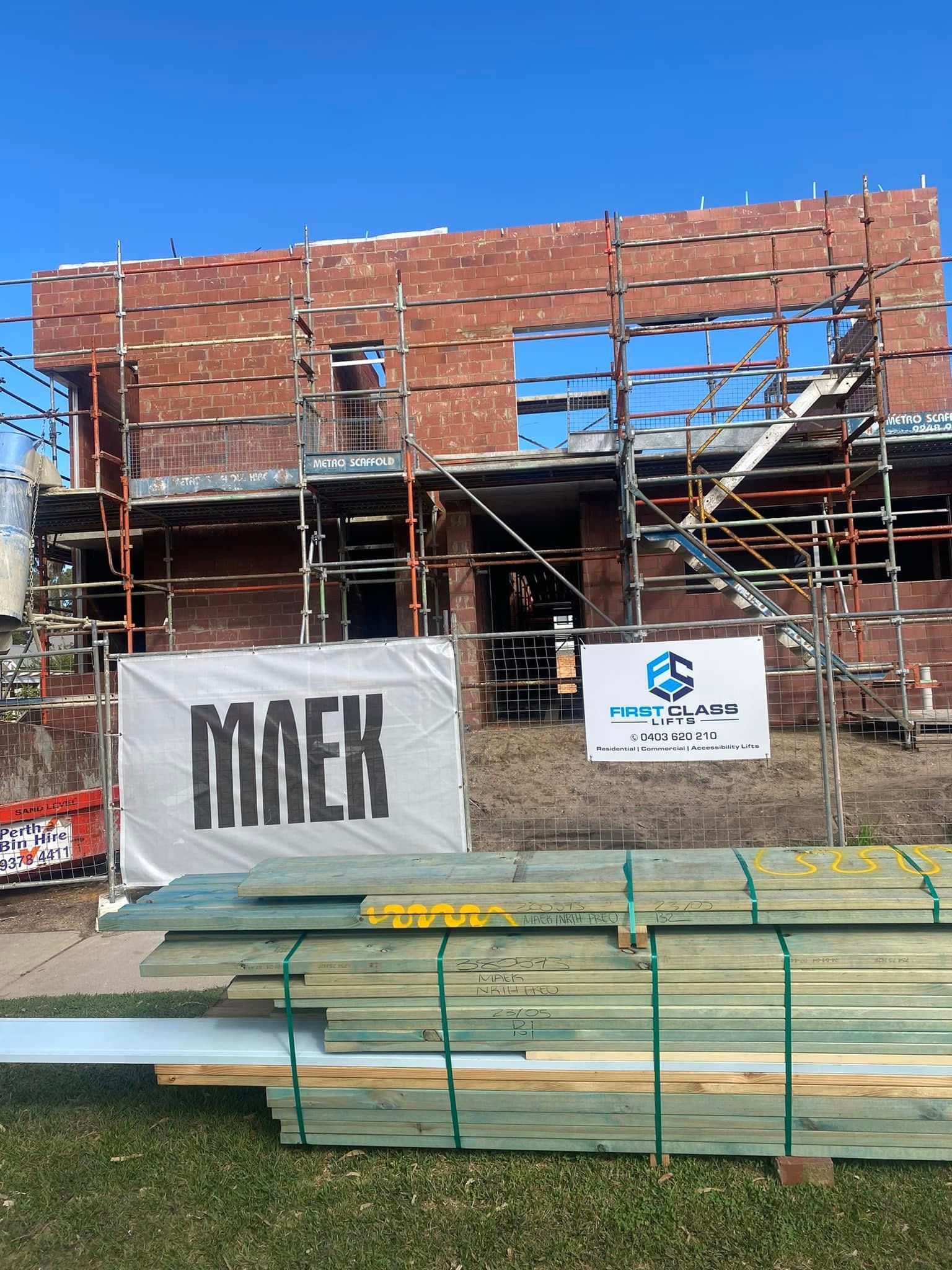 Construction site with red brick building under scaffolding, timber and signs.