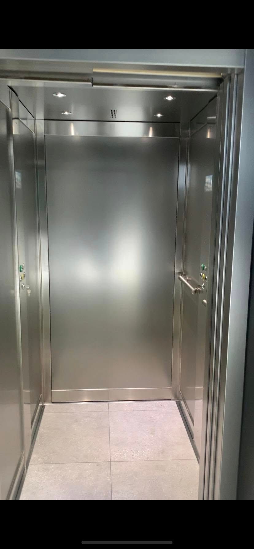 An open elevator with stainless steel walls and a tiled floor.