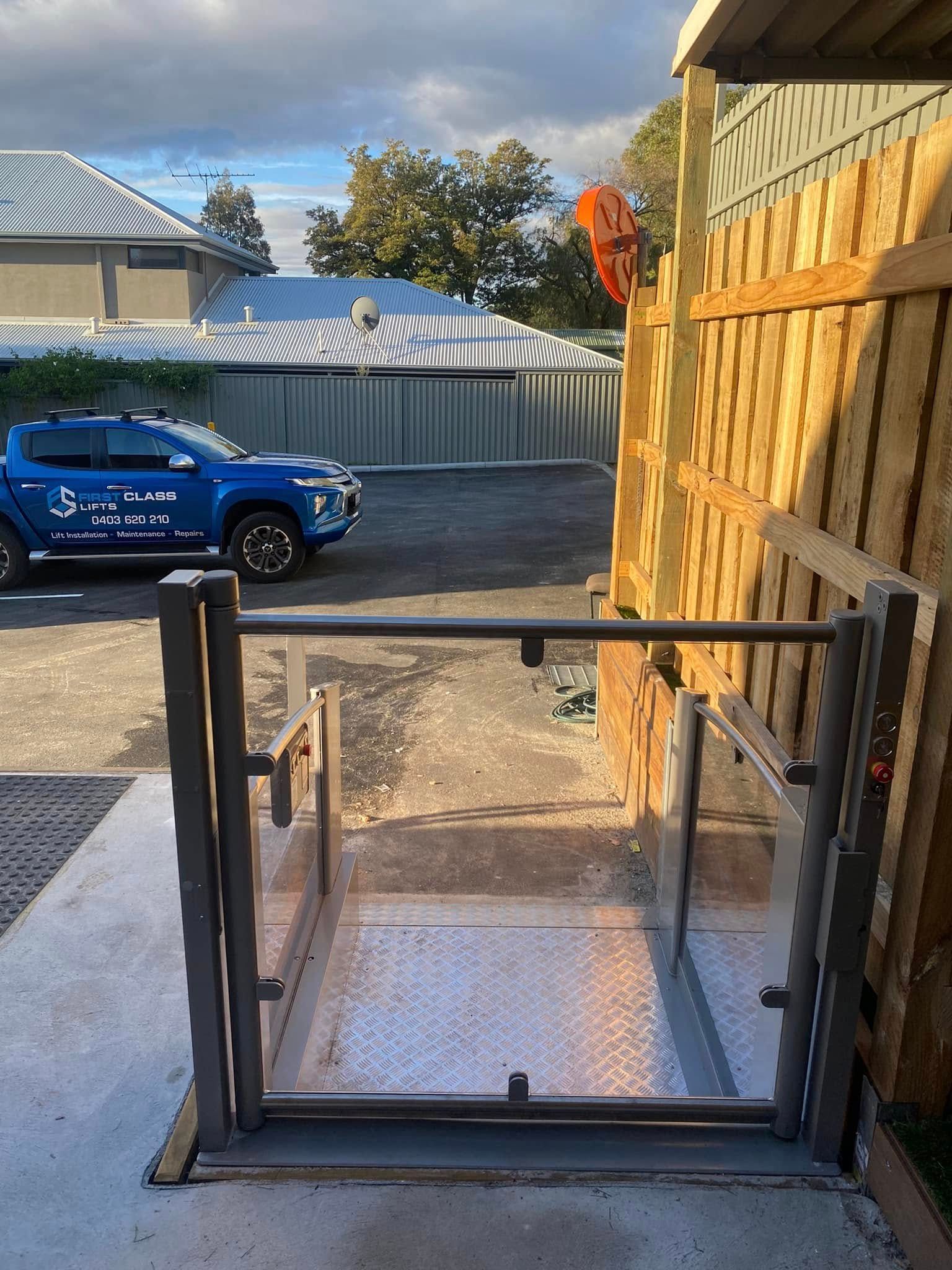 Outdoor wheelchair lift beside a wooden fence and a blue truck.