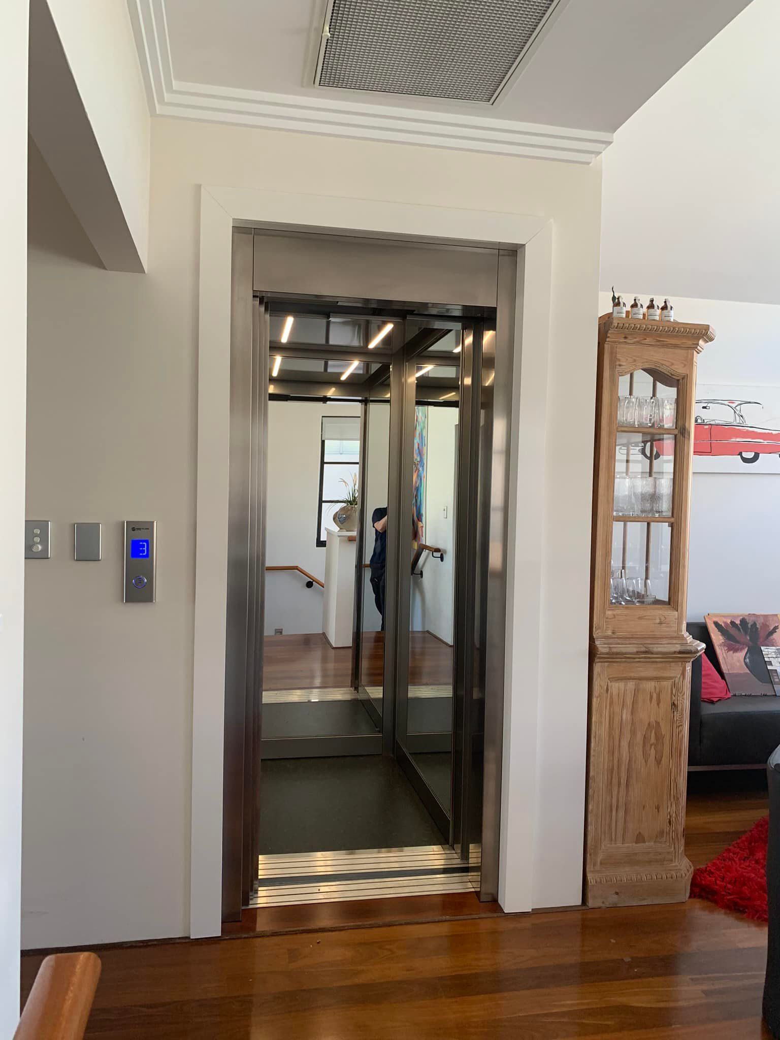 Elevator with stainless steel interior in a home, next to a cabinet.