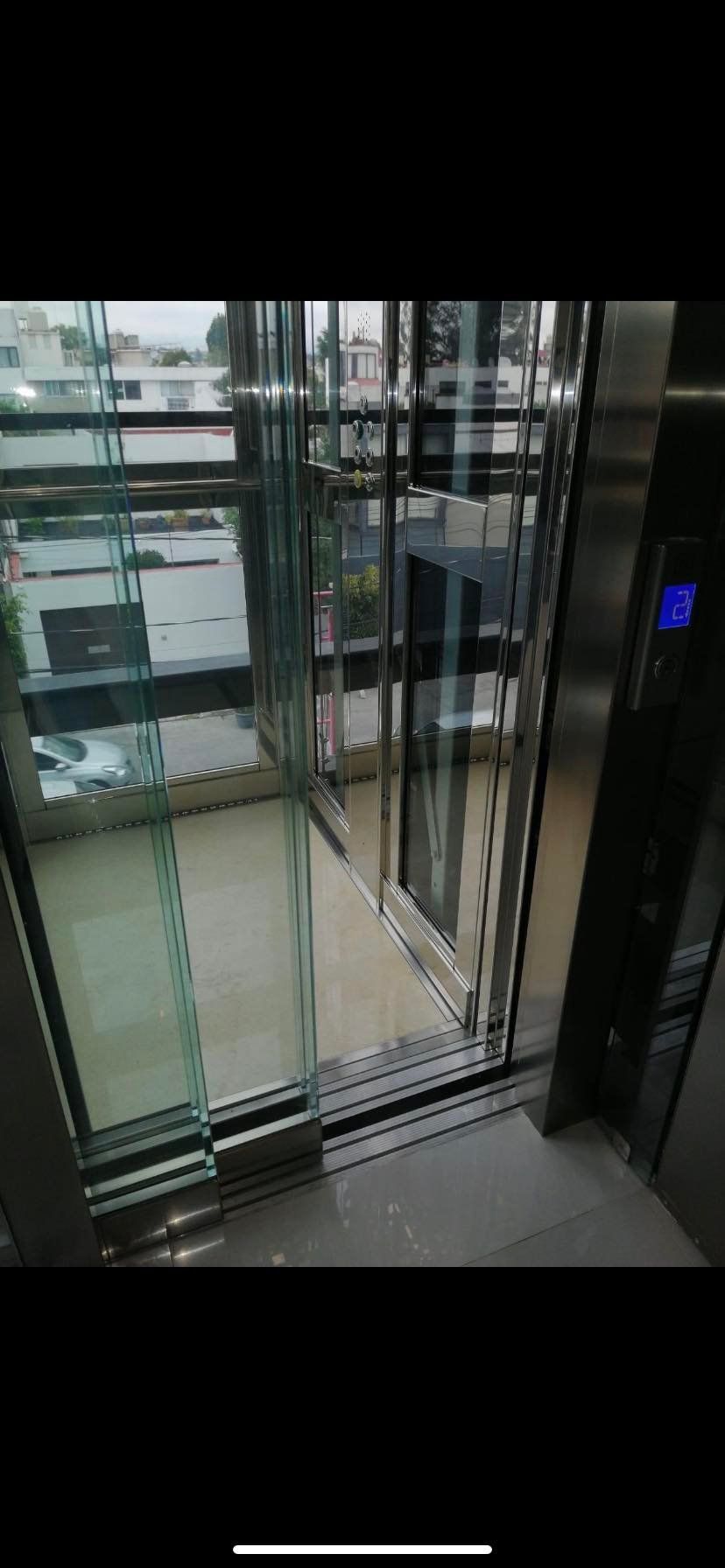 An elevator with glass walls and partially open doors, revealing an outdoor view.