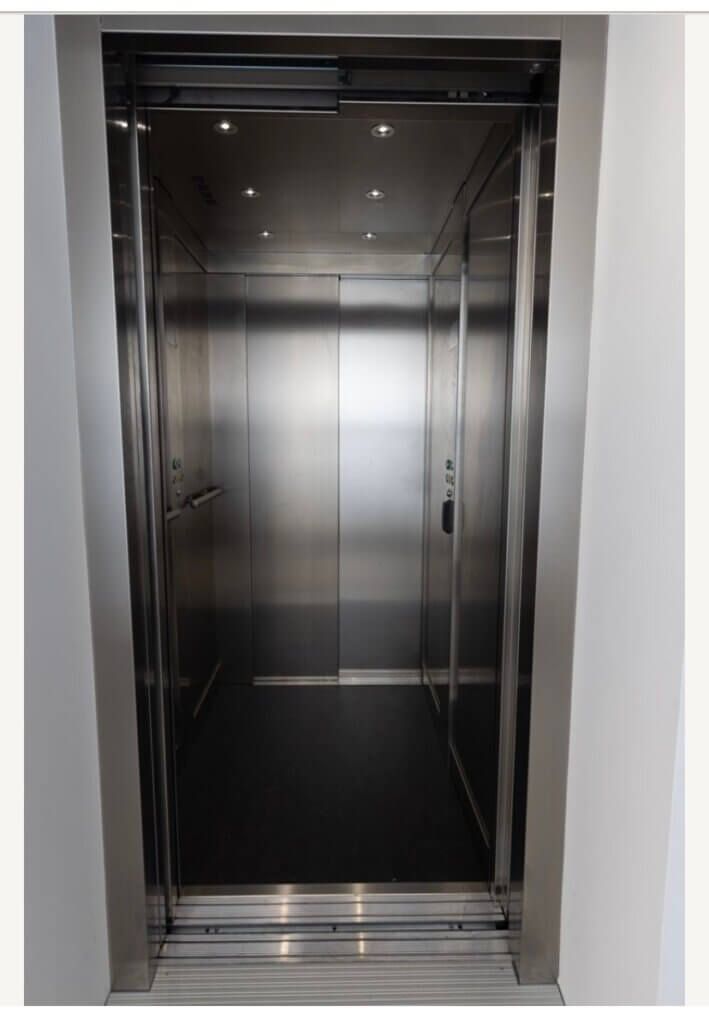 Stainless steel elevator interior, open doors, dark floor, recessed lighting.