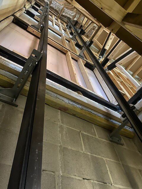 Metal support beams installed along a brick wall within a framed structure, likely for an elevator or lift.