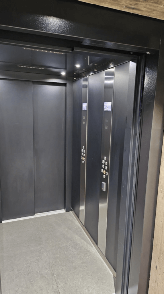 Elevator interior with dark gray walls, stainless steel accents, and control panels.