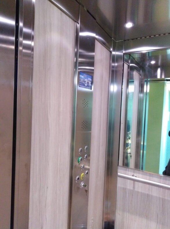 Elevator interior with wood paneling, stainless steel trim, and control panel with buttons.