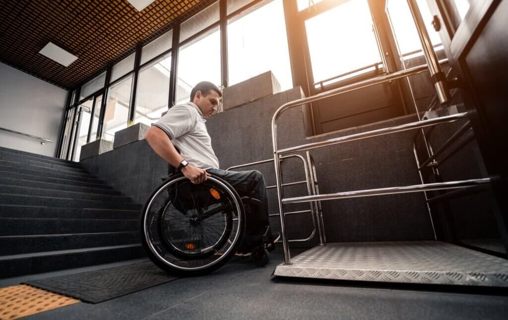 Man in wheelchair at a stair lift platform next to a flight of stairs inside a building.