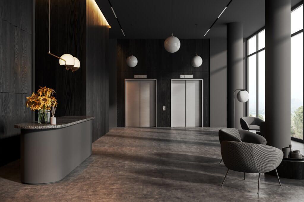 Modern lobby with elevators, dark walls, and gray furniture. Soft lighting and decorative orbs.