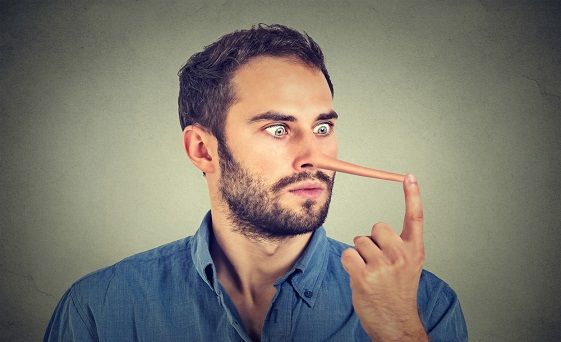 A man with a beard is holding his finger to his nose.