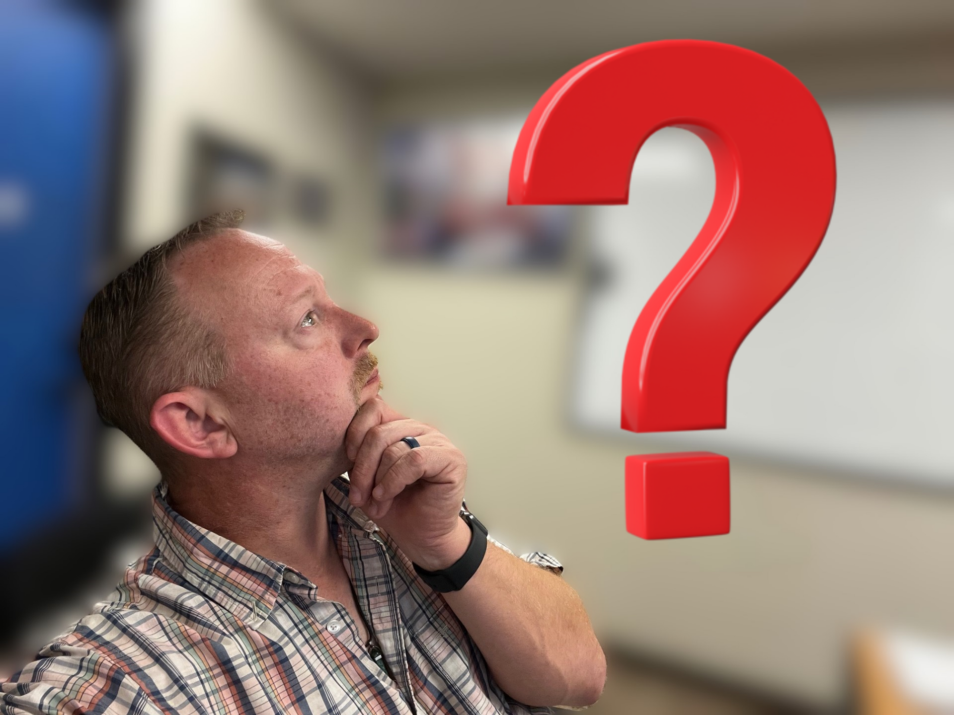 Man looking up, thoughtful expression, near a large red question mark in a classroom setting.