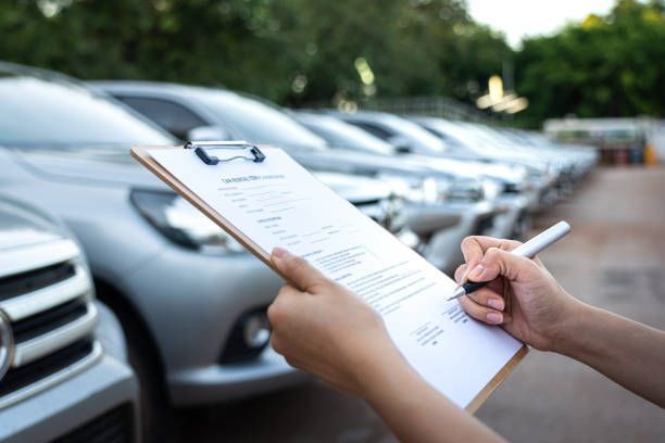A person is writing on a clipboard in front of a row of cars.