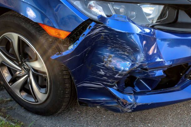 A blue car with a damaged bumper is parked on the side of the road.