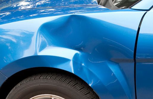 A close up of a blue car with a damaged fender.
