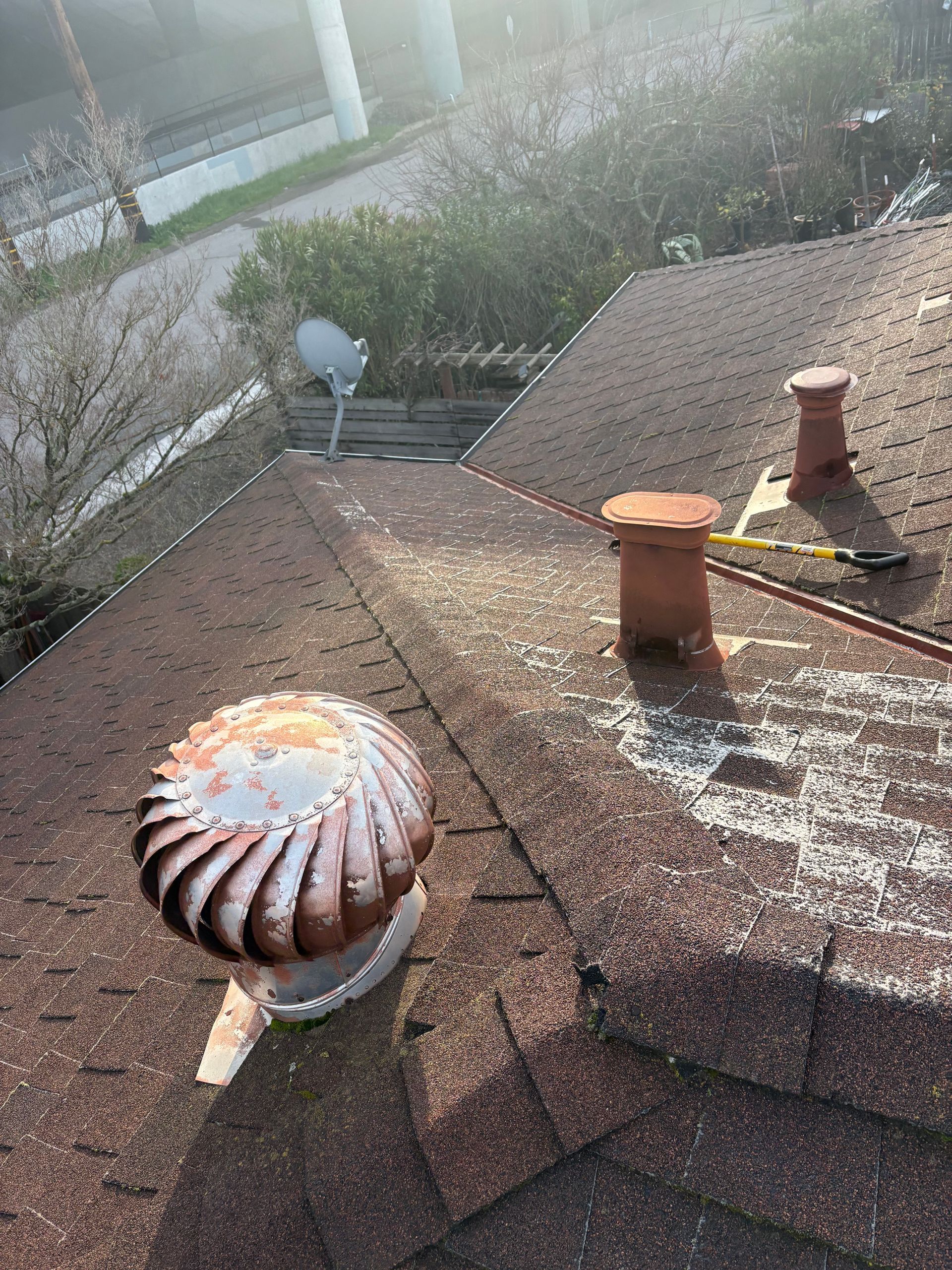 Rooftop with a spinning vent, two chimneys, a satellite dish, and brown asphalt shingles.