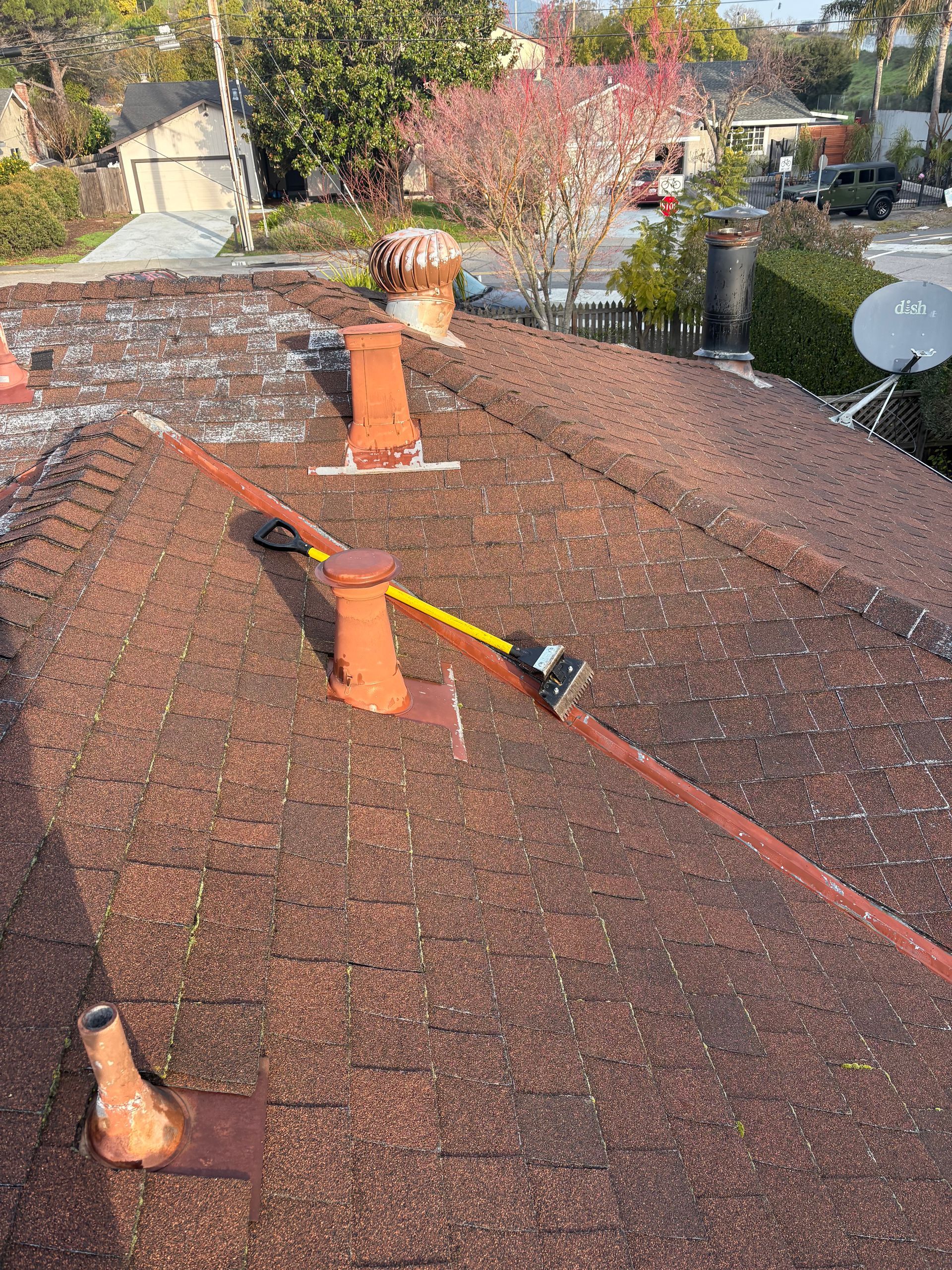 Brown roof with rusty vents, a lightning protection system, and a residential neighborhood in the background.