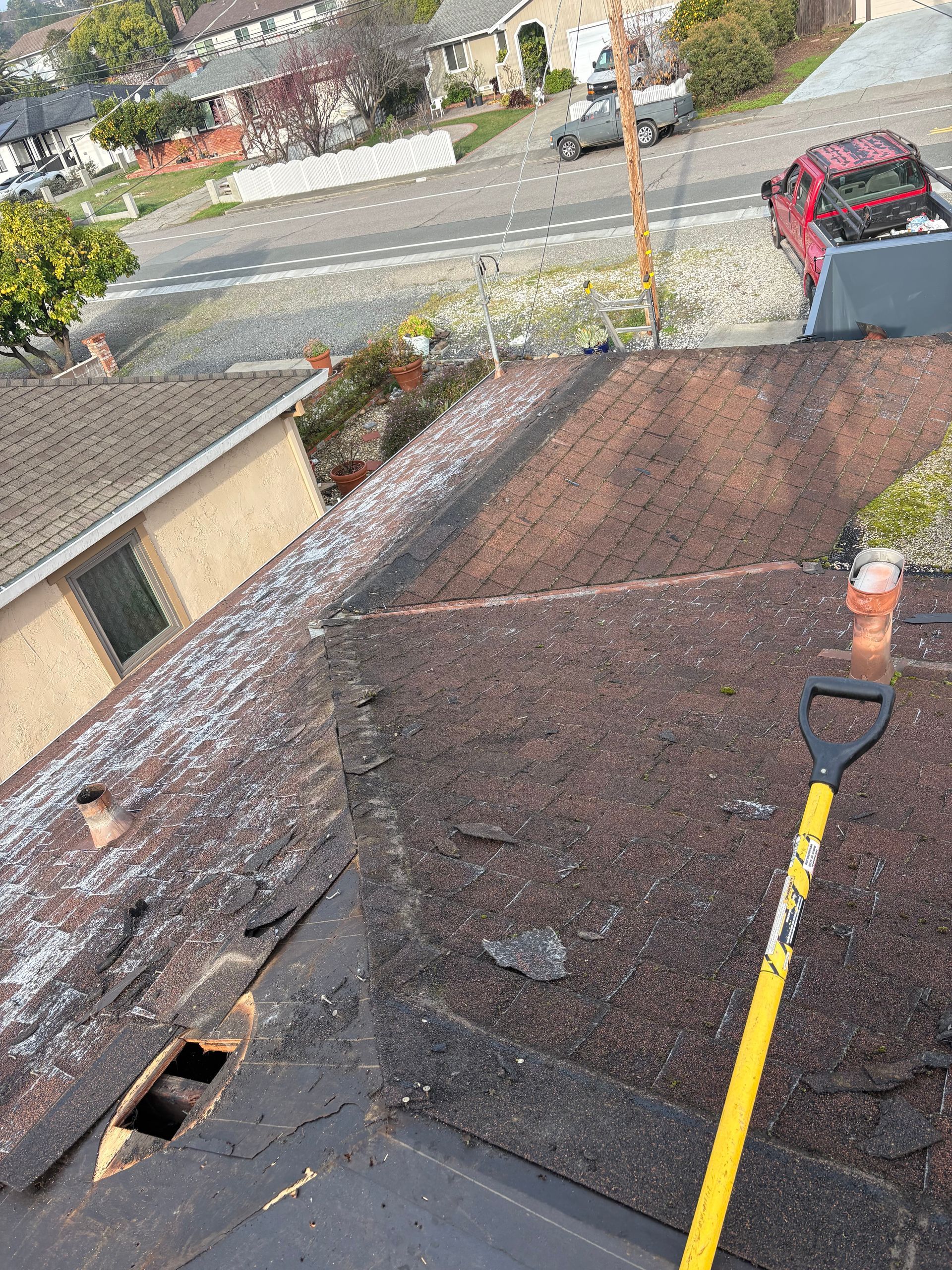 Shovel on a weathered, dark brown rooftop, with visible damage and a street scene in the background.