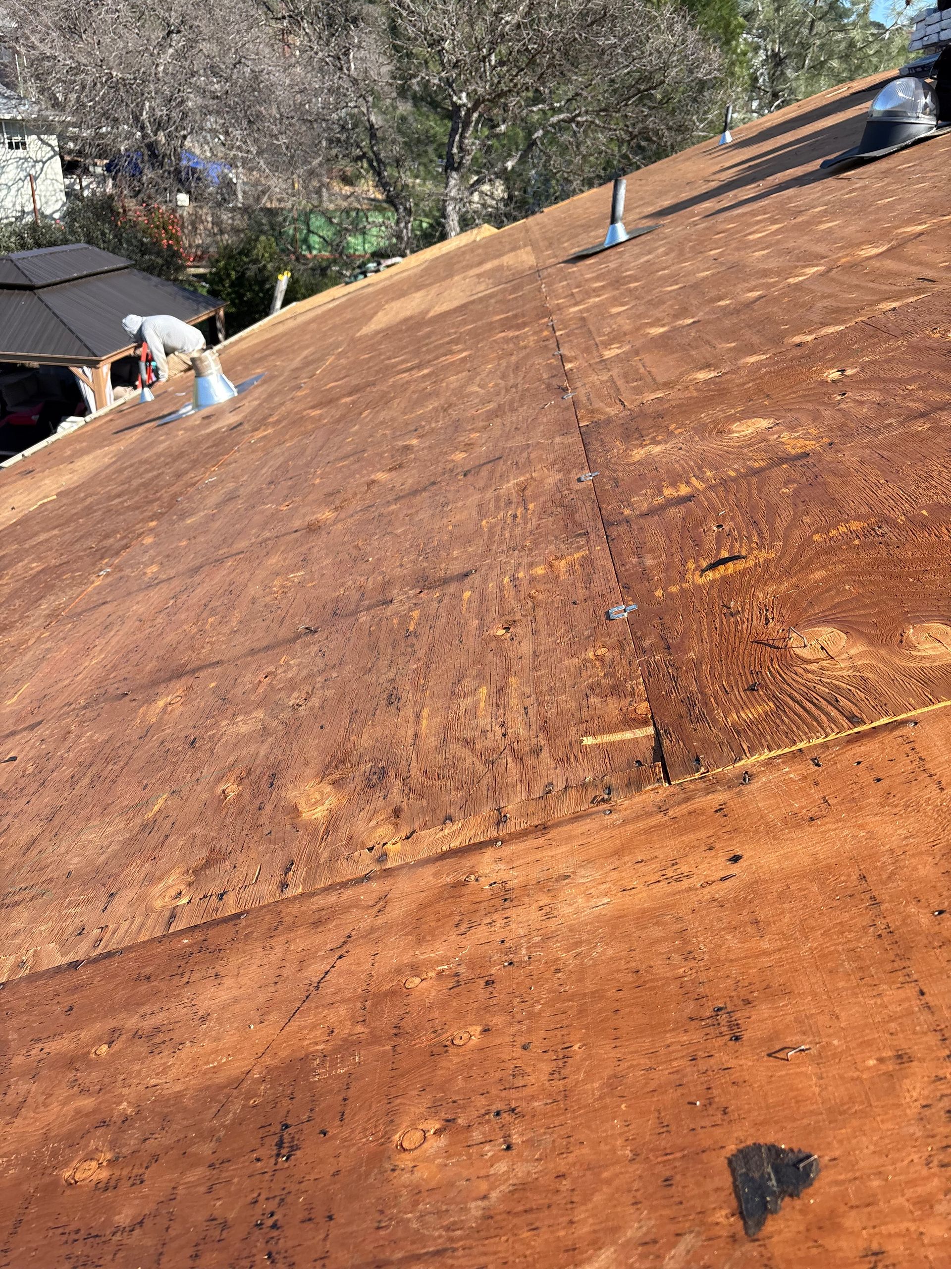 Close-up view of a brown rooftop. Two people are working on the roof. The sky is blue and it is daytime.