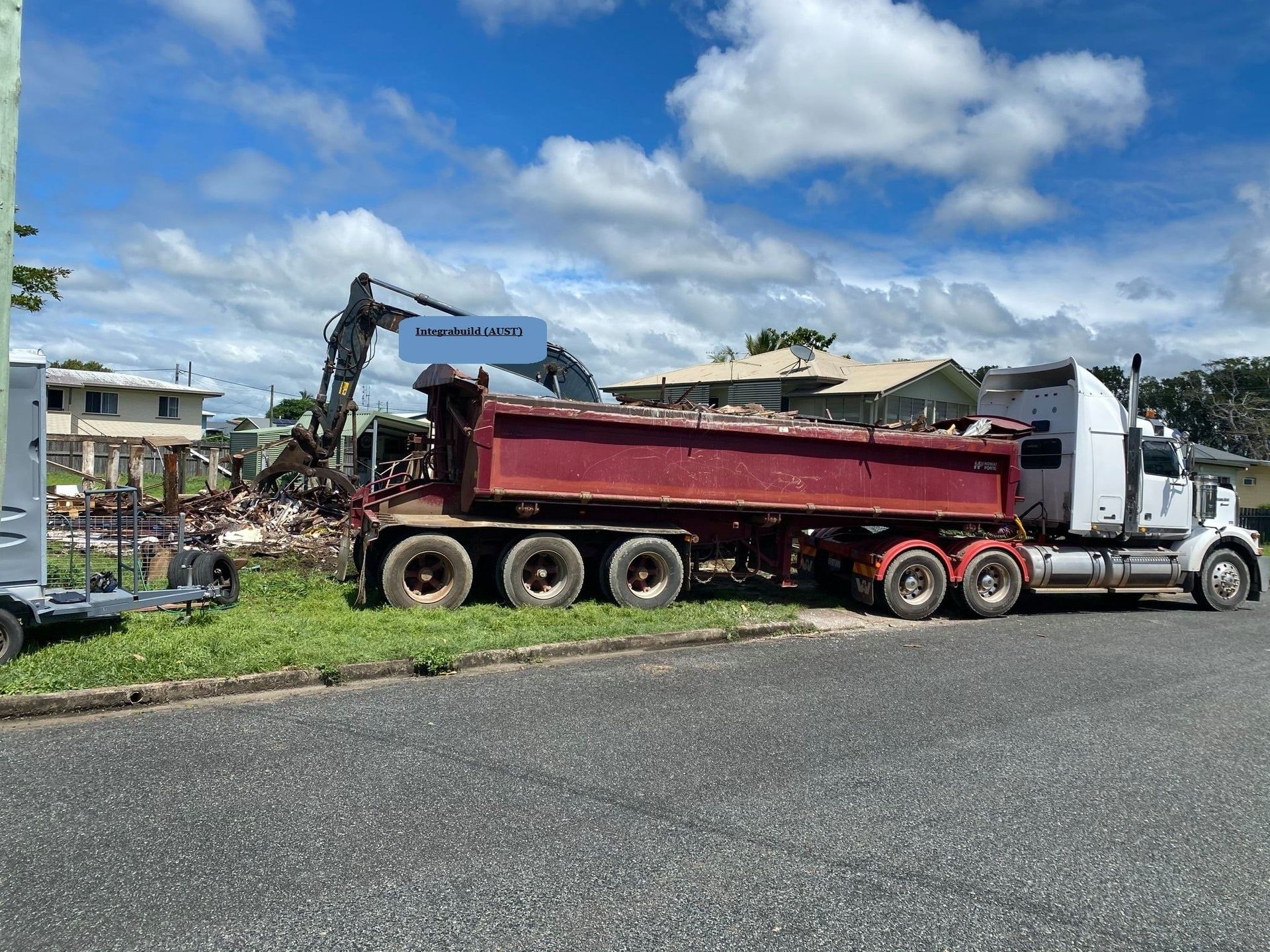 A Large Red Dump Truck is Parked on a Roadside, Being Loaded With Debris — Integrabuild in Bowen, QLD