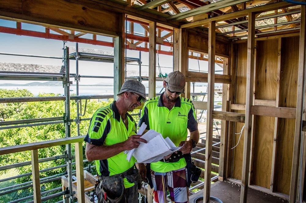 Two Construction Workers Are Looking At A Blueprint In A Building Under Construction — Integrabuild in Bowen, QLD